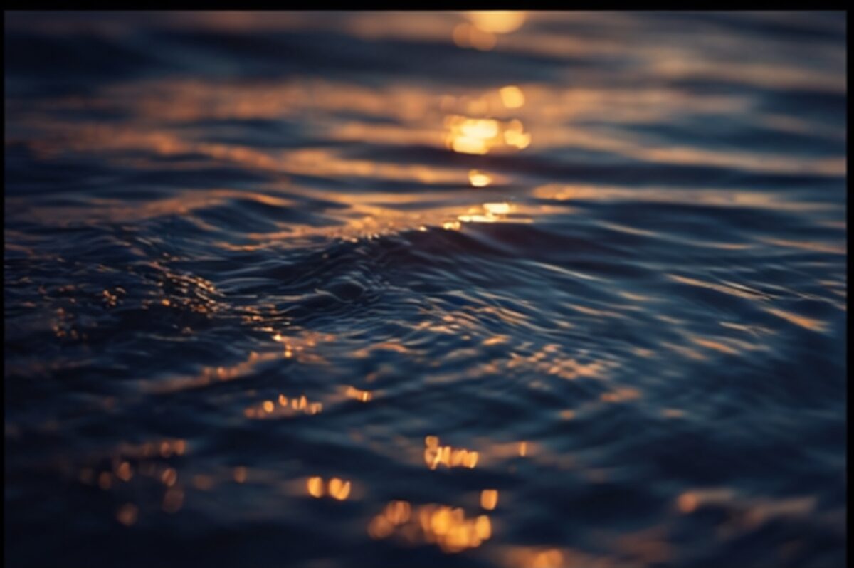 Close-up of warm water surface with amber and teal reflections at dusk